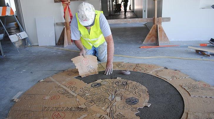 a worker pieces together a mosaic of the pitzer seal on the floor of skandera